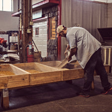 A man pouring a soybean and wheat mixture into a wooden frame