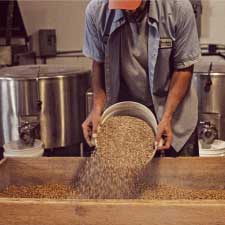 A man using a bucket to pour a soybean and wheat mixture into a wooden frame