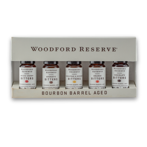 Woodford Reserve Bourbon Barrel Aged Bitters gift set in a beige presentation box, containing five small amber glass bottles with white labels.