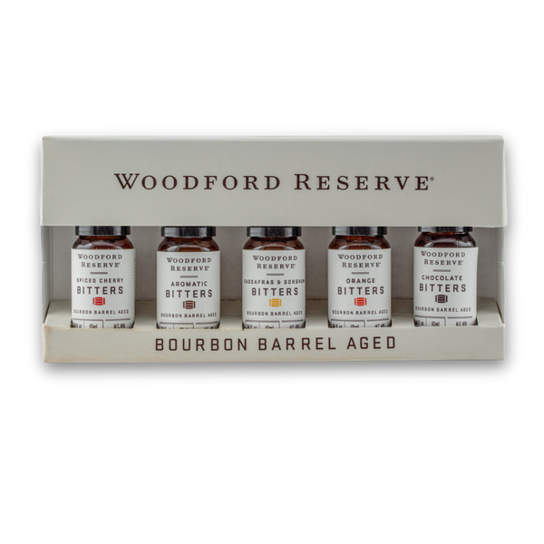 Woodford Reserve Bourbon Barrel Aged Bitters gift set in a beige presentation box, containing five small amber glass bottles with white labels.