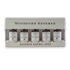 Woodford Reserve Bourbon Barrel Aged Bitters gift set in a beige presentation box, containing five small amber glass bottles with white labels.