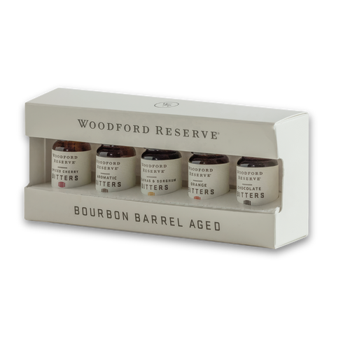 Woodford Reserve Bourbon Barrel Aged bitters set in a white presentation box, containing four small bottles with dark bitters visible through clear windows.