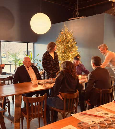 Group of people gathered around a wooden table in a cozy café decorated with a Christmas tree and warm lighting.