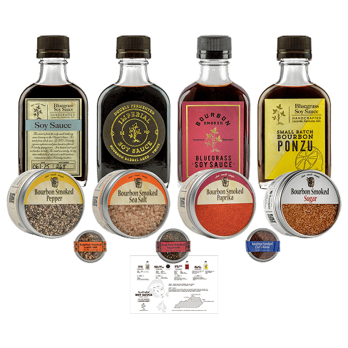 A product lineup of Bluegrass Sea Sauce Company's artisanal condiments and seasonings, including soy sauce, bourbon smoked soy sauce, soy sauce ponzu, sea salt, pepper, paprika, and sugar, arranged on a clean white background.