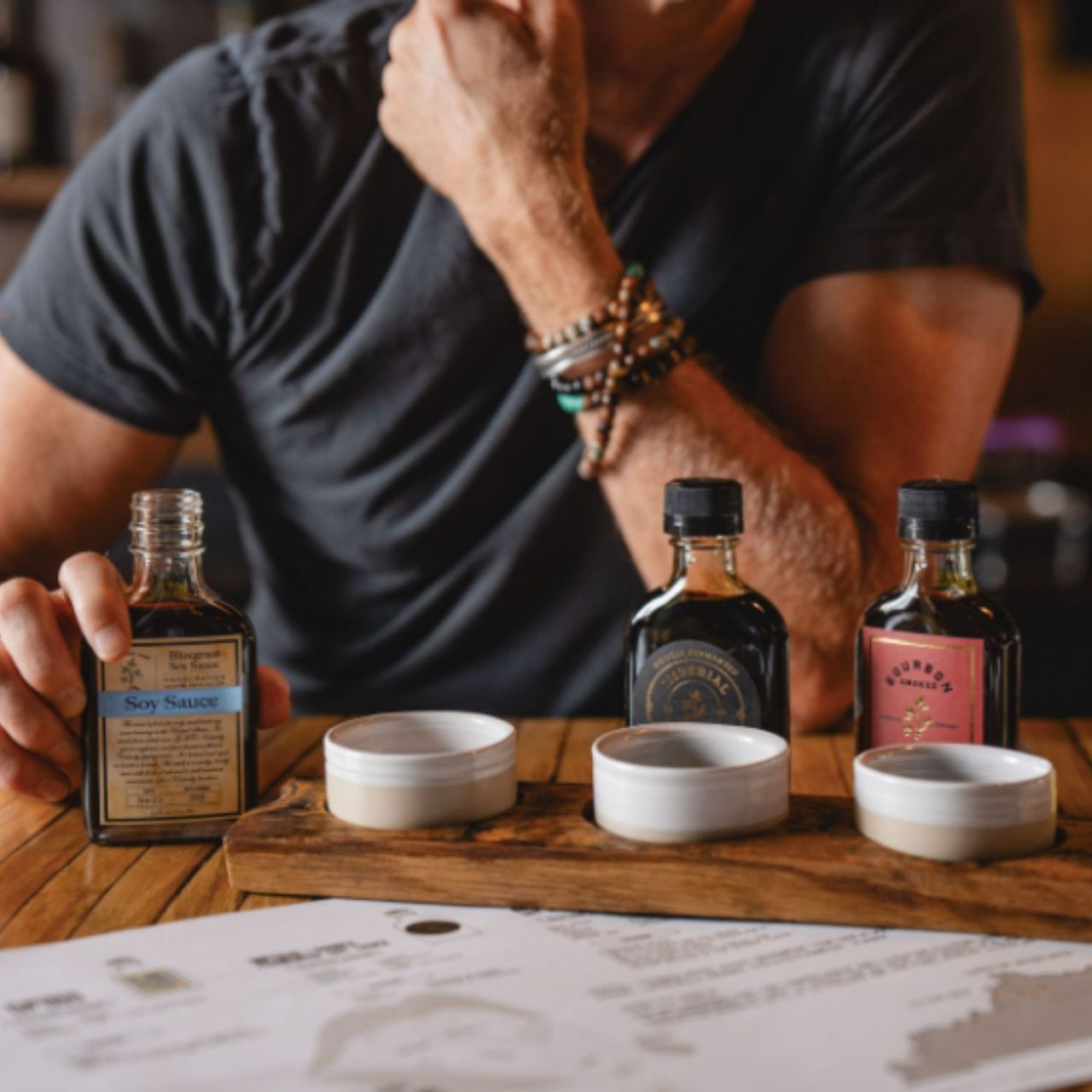 A guest at a tasting table with Bourbon Barrel Foods soy sauce and bitters bottles and a flight of tasting cups