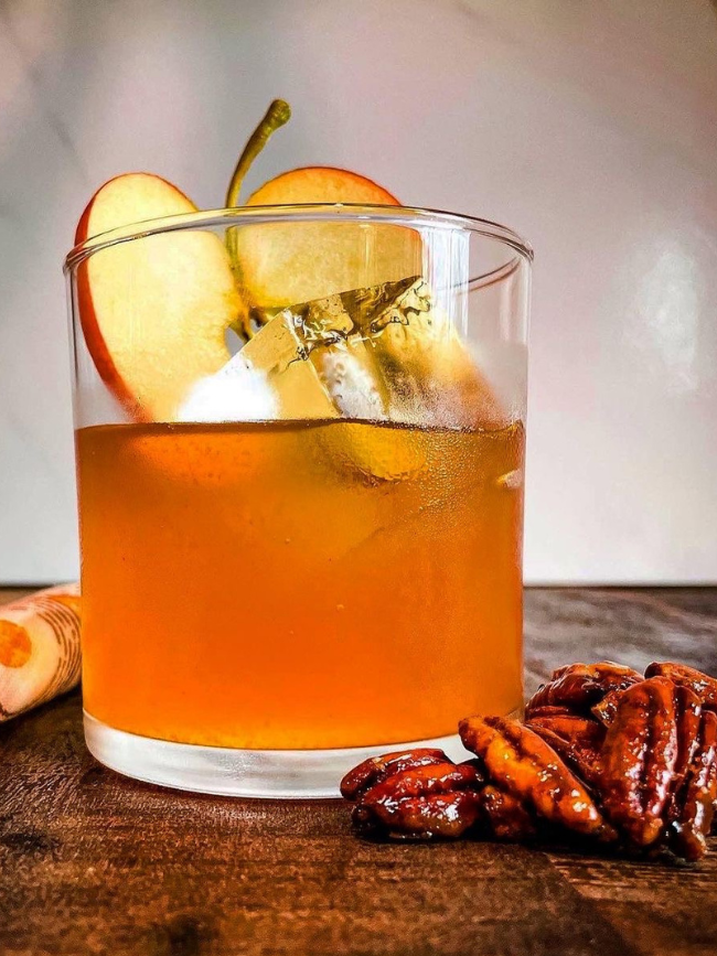 An Old Fashioned cocktail shown with an ice cube and apple slice 