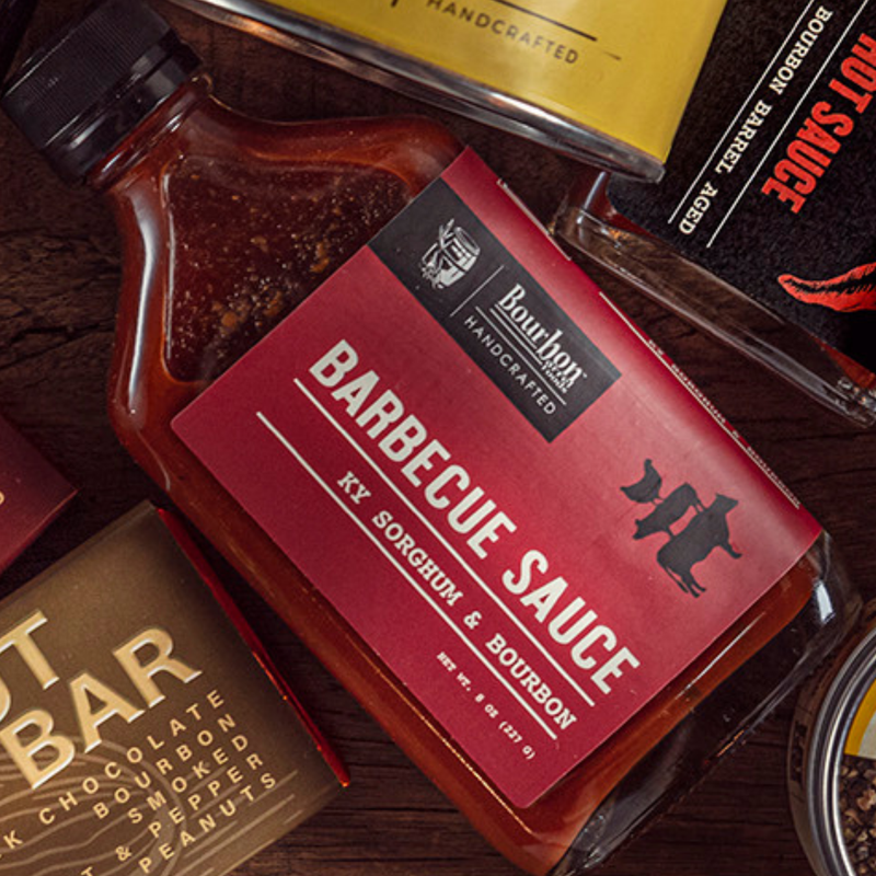 Bourbon Barrel Foods barbecue sauce bottle with a red label on a wooden surface.