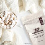 Bourbon Barrel Foods Dark Hot Chocolate with Bourbon Smoked Sea Salt on a cozy blanket with a ready to sip serving filled to the rim with marshmallows.