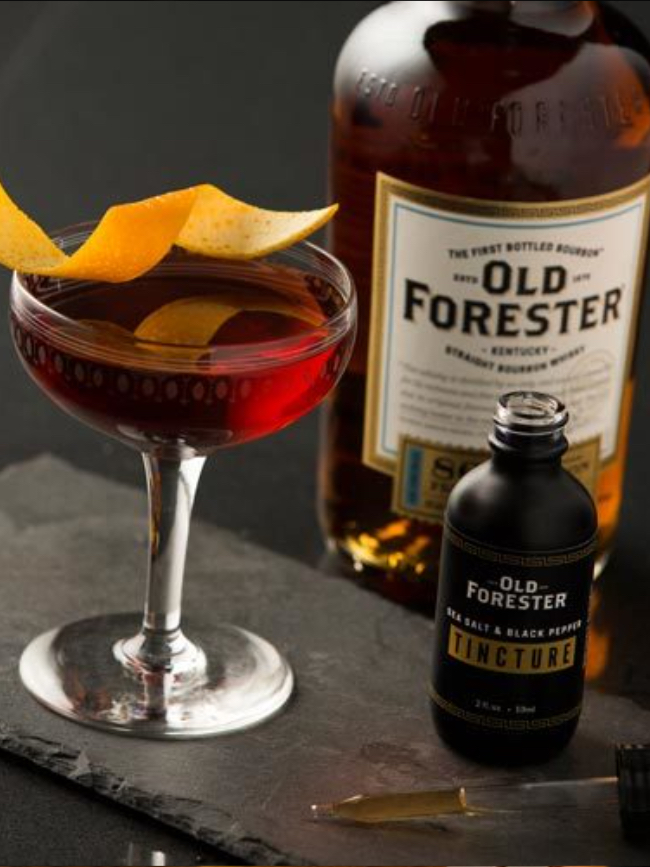 Old Forester Boulevardier Cocktail next to a bottle of Tincture and in front of a bottle of Old forester