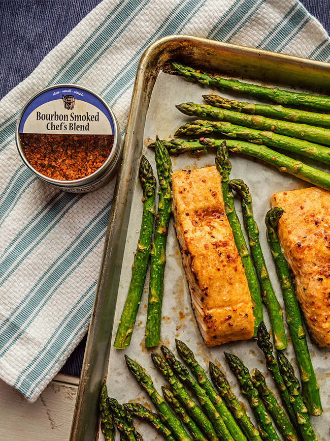 Sheet pan with Salmon and asparagus next to a tin of Bourbon smoked chef's blend spices