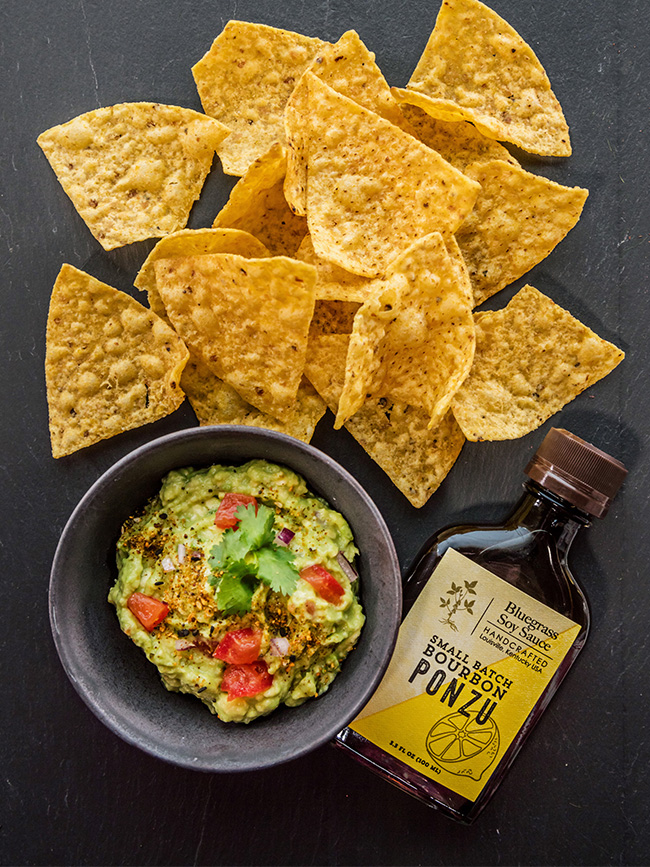 Tortilla chips with Guacamole next to a bottle of bluegrass soy sauce small batch bourbon ponzu