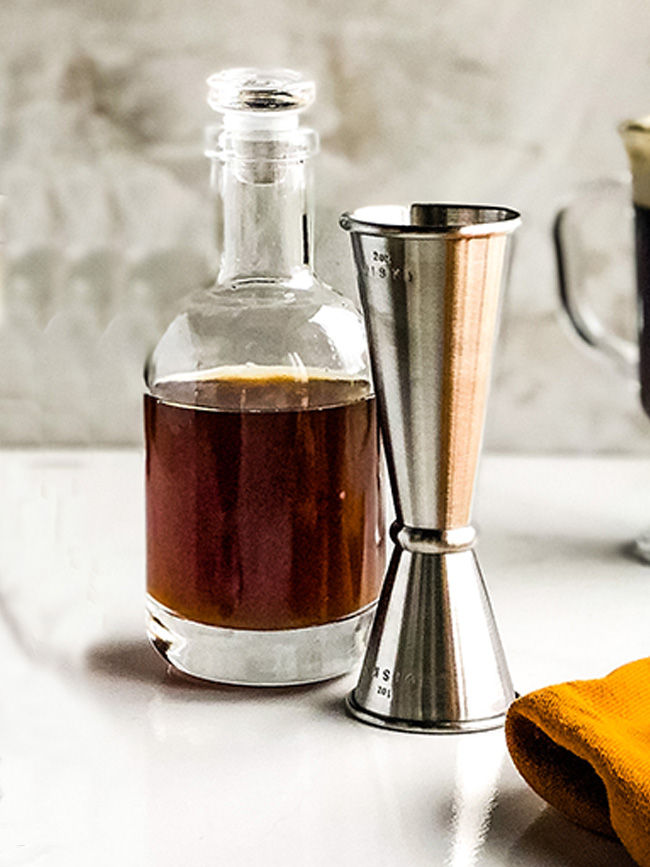Bottle of Bourbon Smoked Simple syrup next to a jigger
