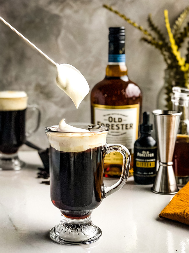 Coffee with whipped cream on top in front of a bottle of old forester bourbon and bitters